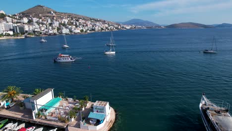 Tour-Boats-Gracefully-Enter-the-Tranquil-Port-of-Coastal-Saranda,-Amidst-Boats-and-Promenade,-Perfect-for-a-City-Holiday