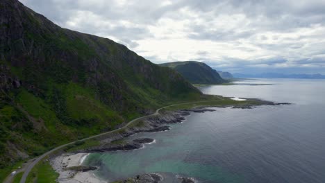 Aerial-forwarding-dolly-shot-of-of-the-scenic-driving-route-on-Andøya-coast-with-mountains-and-rocky-coast-green-in-the-summer-months