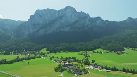 Cinematic-drone-soars-backward-above-scenic-rural-area,-unveiling-famous-Drachenwand-mountain-near-Mondsee,-Austria
