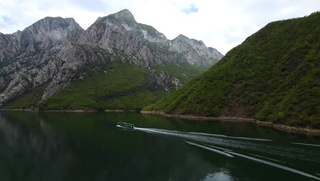 Barco-Navegando-En-Las-Tranquilas-Aguas-Del-Lago-De-Koman-En-Albania,-Reflejando-Majestuosas-Montañas-En-Un-Sereno-Paisaje-Acuático