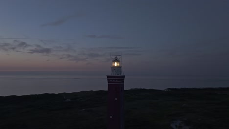 Orbit-shot-of-Lighthouse-Westhoofd-with-light-on-during-sunset,-aerial