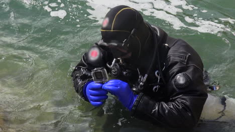 Technical-diver-in-gear-inspects-underwater-camera-at-chaotic-river
