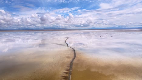 Drone-shot-flying-over-the-Salinas-Grandes-salt-lake-on-the-border-of-Salta-and-Jujuy,-Argentina-following-a-dirt-path