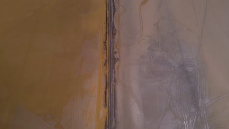 Drone-shot-flying-over-a-dirt-path-panning-up-to-reveal-the-Salinas-Grandes-salt-lake-on-the-border-of-Salta-and-Jujuy,-Argentina