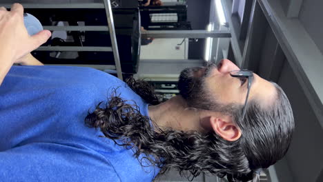 Latino-Mann-Mit-Bart-Und-Langen-Haaren,-Der-Im-Fitnessstudio-Feuchtigkeit-Spendet
