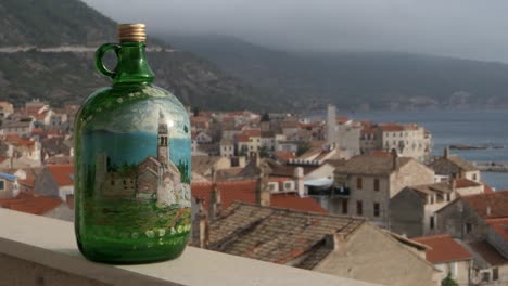 Botella-De-Vino-Tradicional-En-El-Balcón-Con-Vistas-Al-Casco-Antiguo,-Las-Montañas-Y-El-Mar.