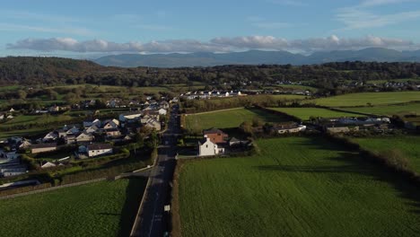 Aerial-view-circling-over-small-town-Welsh-community-farmland-with-Snowdonia-mountain-range-on-the-horizon