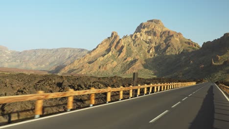 Conduciendo-Por-Una-Carretera-Con-Una-Valla-Al-Borde-De-La-Carretera-Que-Va-Hacia-La-Montaña-Durante-La-Puesta-De-Sol,-Pov