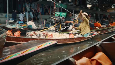 Old-woman-struggles-to-paddle-her-wares-among-motorized-long-tail-boats-in-a-canal