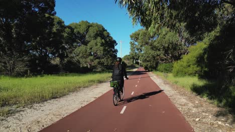 Una-Mujer-Andando-En-Bicicleta-En-Una-Línea-Roja-De-Bicicletas-Dentro-De-Un-Parque-Público-Verde-En-Un-Día-Soleado-De-Cielo-Azul-En-Coogee,-Perth,-Australia-Occidental