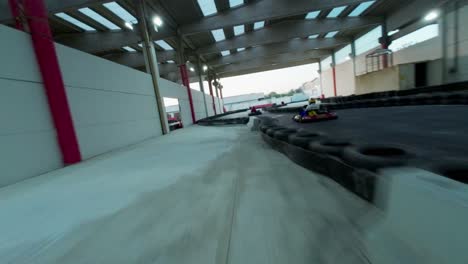 Fpv-racing-drone-flying-over-pilots-driving-fast-go-karts-on-indoor-and-outdoor-track-of-kartdrome-in-Italy