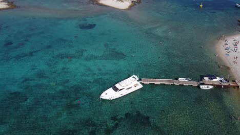 Yacht-speedboat-moored-at-beach-jetty-in-Budikovac-blue-lagoon,-croatia-with-people-swimming