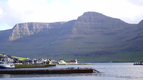Hvannasund-red-roof-church-at-Vidoy-fjord-with-scenic-mountainous-landscape-behind,-Faroe-Islands