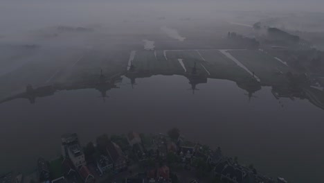 Reveal-shot-of-Zaanse-schans-Holland-windmills-during-sunrise-with-fog,-aerial