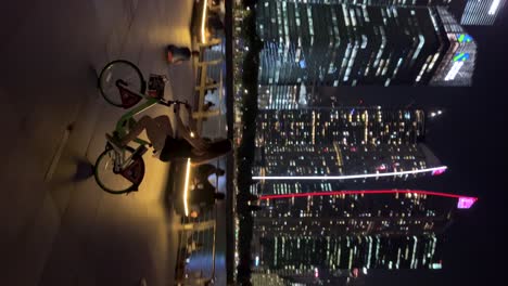 Young-lady-cycling-through-Marina-Bay,-Singapore,-with-the-breathtaking-Marina-Bay-Sands-and-skyscrappers-in-the-background-at-night,-showcasing-stunning-architecture-and-views