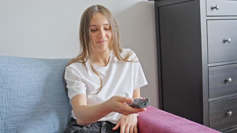 Woman-sitting-happily-on-couch-while-pressing-buttons-of-remote-control-towards-the-TV-at-home,-static-closeup