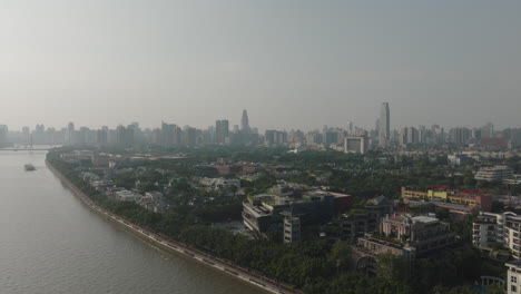 Aerial-of-suburban-houses-next-to-the-river-looking-at-city-skyline-of-Guangzhou-city,-China