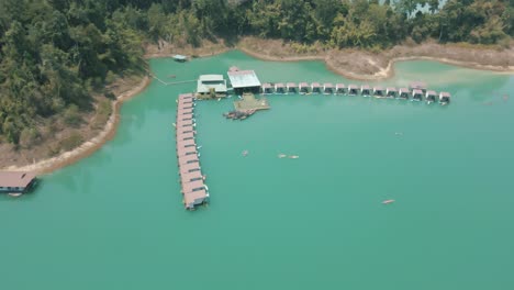 Impresionantes-Imágenes-De-Drones-De-Varias-Personas-Navegando-En-Kayak-Junto-A-Los-Bungalows-Flotantes-En-El-Parque-Nacional-De-Khao-Sok,-Tailandia