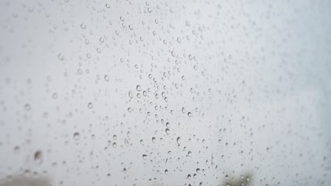 A-close-up-focus-of-heavy-rain-drops-is-seen-through-a-window-glass