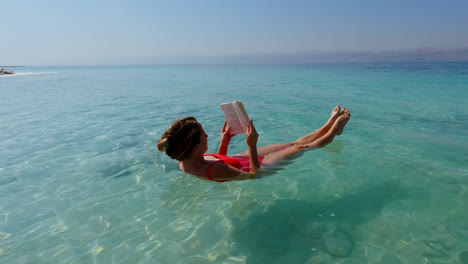 Peaceful-Young-Woman-Floating-in-the-Dead-Sea-wearing-Red-Swimsuit-and-Reading-a-Book