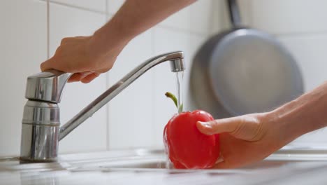 Man-rinsing-a-bell-pepper-under-the-kitchen-faucet