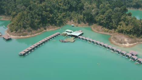 Imágenes-épicas-De-Drones-De-Personas-Navegando-En-Kayak-Junto-A-Los-Bungalows-Flotantes-En-El-Parque-Nacional-De-Khao-Sok,-Tailandia