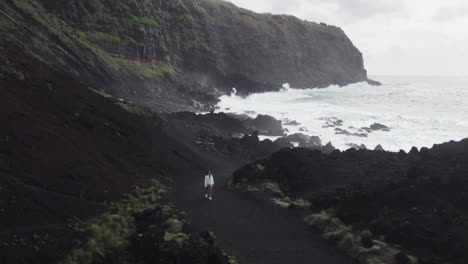 Girl-walking-on-Ponta-da-Ferraria's-black-sands,-Azores---Aerial