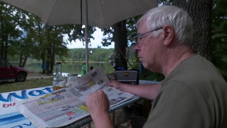 Grey-haired-man-sits-outdoors-in-woodland-scene-reading-local-newspaper