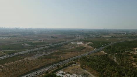 A-main-road-in-central-Israel,-a-road-that-crosses-agricultural-fields-and-a-natural-forest,-on-the-horizon-of-the-towers-of-Tel-Aviv