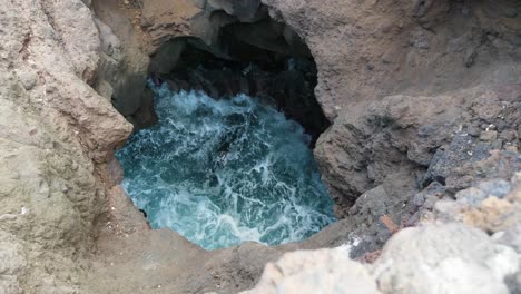 Ocean-waves-crashing-and-splashing-beneath-a-hole-in-the-volcanic-coastal-rocks-of-los-Hervideros-in-Lanzarote