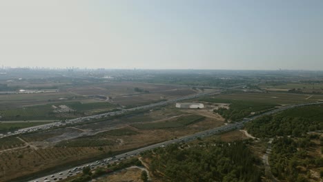 A-main-road-in-central-Israel,-a-road-that-crosses-agricultural-fields-and-a-natural-forest,-on-the-horizon-of-the-towers-of-Tel-Aviv