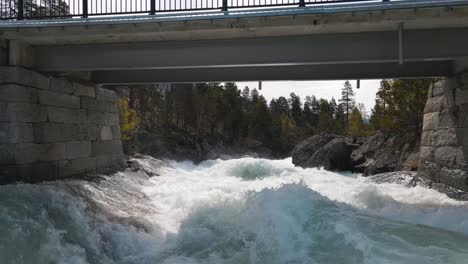 Srone-footage-following-along-fast-flowing-river,-under-bridge-in-Norway,-Billingen