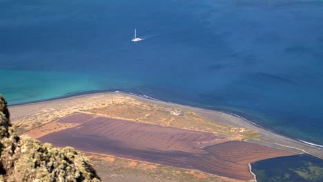 Vista-Desde-Arriba-Del-Mirador-Del-Río-En-Lanzarote-Mientras-Un-Barco-Blanco-Cruza-El-Mar-Frente-A-La-Costa