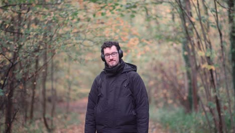 Cheerful-young-German-gentleman-with-glasses-and-beard,-stands-amidst-the-hues-of-an-autumnal-European-mixed-forest,-grinning-warmly-and-offering-a-friendly-greeting