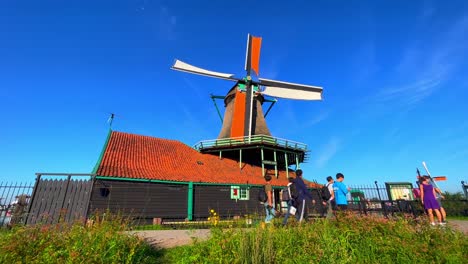 Low-angle-shot-of-a-windmill-as-people-pass-by-in-Zaanse-Schans,-Netherlands---Blue-sky-background-with-windmill