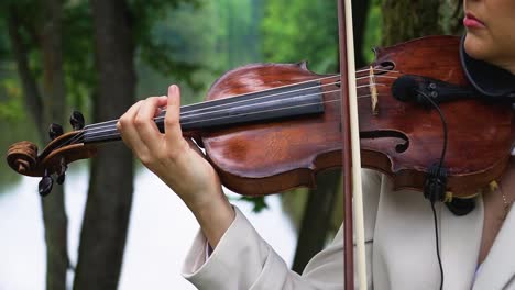 Closeup-footage-of-a-female-violinist-playing-violin-in-the-green-park-by-the-lake-in-summer-time