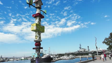 Sculptures-and-people-in-Downtown-coastal-promenade-the-Embarcadero-with-fishing-boat-and-marina,-navy