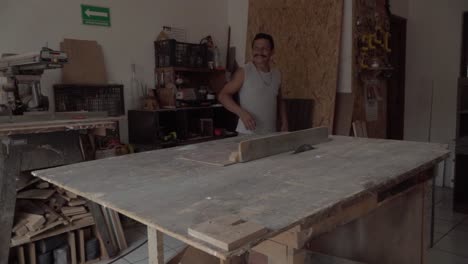 A-middle-aged-mustached-man-in-a-carpentry-shop-smiling-as-he-turns-around-and-walks-away