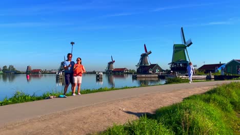 Tourists-walk,-take-selfies,-and-enjoy-the-beautiful-sight-of-windmills-at-sunrise-in-Zaanse-Schans,-Netherlands