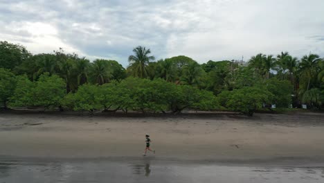 Solo-woman-runs-along-waters-edge-on-beach-in-Guanacaste-Costa-Rica,-aerial