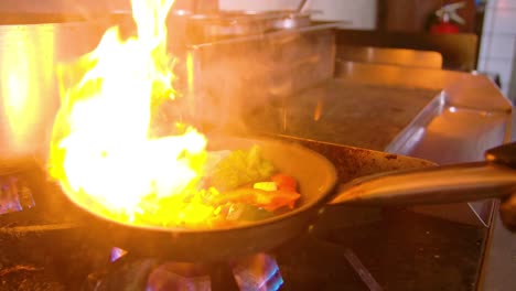 Chef-dropping-fresh-green-vegetables-in-frying-pan,-big-fire-flames-shooting-up