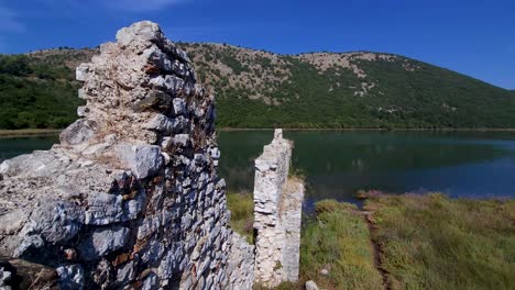 Viejos-Muros-De-Piedra-En-Ruinas-Y-Un-Antiguo-Castillo-Descansan-A-Orillas-Del-Lago-De-Butrint,-Una-Maravilla-Arqueológica