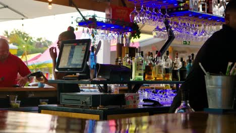 Bartenders-working-behind-wooden-bar-top-with-alcoholic-drinks-and-register