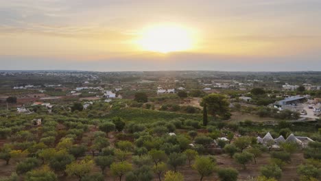 Aerial-landscape-view-of-a-rural-village-with-white-buildings,-surrounded-by-olive-trees,-in-the-italian-countryside,-at-sunset