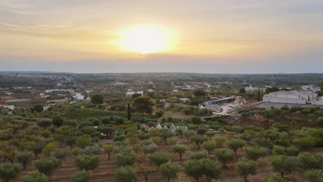 Aerial-landscape-view-over-a-rural-village-with-white-buildings,-surrounded-by-olive-trees,-in-the-italian-countryside,-at-sunset