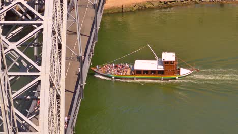 Boat-with-tourists-passing-near-the-Dom-Luís-I-bridge-in-Porto,-Portugal