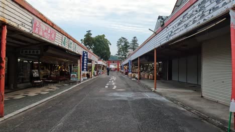 Caminando-Por-La-Carretera-Principal-Frente-A-Una-Gran-Puerta-Torii-Y-Compras-En-El-Santuario-Yutoku-Inari-En-Kyushu,-Japón