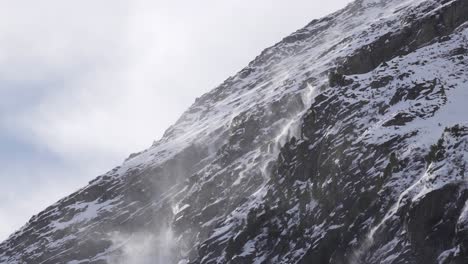 Close-up-of-snow-getting-blown-off-a-mountain-cliff-ridge-on-a-snowy-rocky-glacier-slope