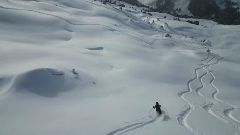 Antena-Siguiendo-A-Un-Joven-Esquiador-Deportivo-Descendiendo-La-Pendiente-De-La-Cordillera-Del-Glaciar-Cubierto-De-Nieve-En-Un-Paisaje-Alpino-Nevado