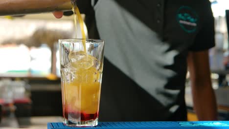 Bartender-pouring-yellow-drink-into-glass-on-wooden-bar-top,-hurricane-cocktail